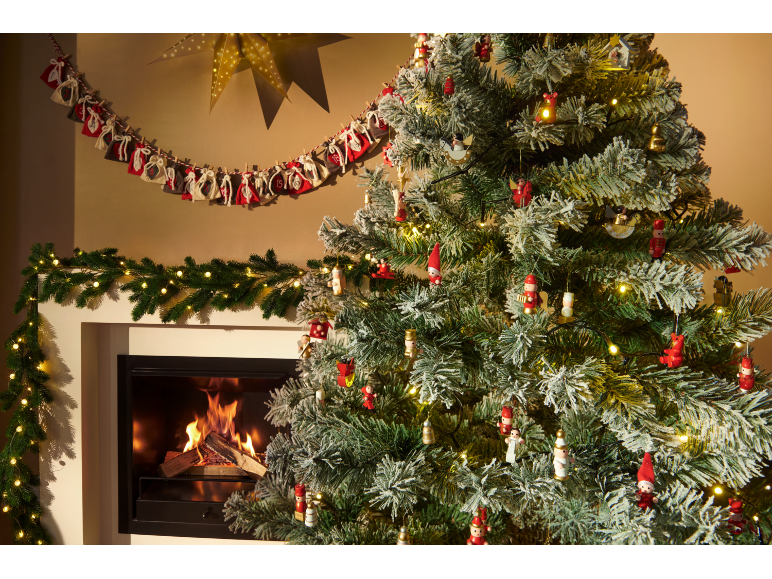 Snowy Christmas tree with decorations and a lit fireplace, garland, and Advent calendar.