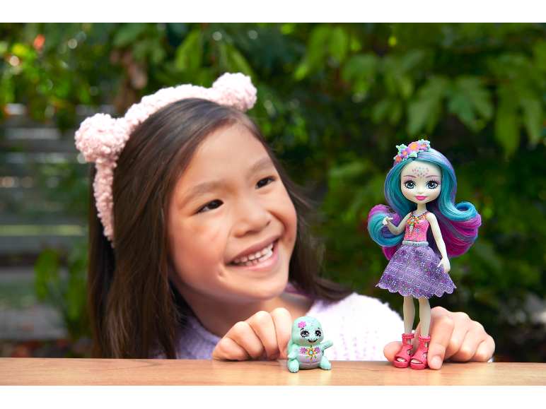 Smiling girl with a doll and a small toy on a wooden surface.