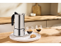Stainless steel espresso maker with two espresso cups and a biscotti on a marble tray.