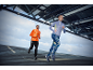 Two runners in long-sleeved athletic tops and leggings, running outdoors under a metal structure.