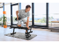 Man exercising with a dumbbell on a workout bench in a bright room.
