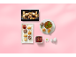 Baklava assortment box, baklava and pomegranate seeds on platter, cup of tea and bowl of pomegranate seeds on pink background.