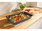 Baking pan with roasted gnocchi, tomatoes, and herbs on a wooden kitchen counter.