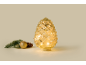Illuminated decorative glass pine cone with Christmas decorations next to it.