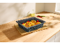 Baking dish with grilled corn, chili, and oil on a wooden countertop.