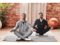 Two men in tracksuits meditate on yoga mats in a room with a brick wall.