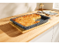 A baking tray with an almond cake on a wooden counter, with a piece cut out.