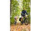 Man and woman cycling on a forest path covered with autumn leaves.