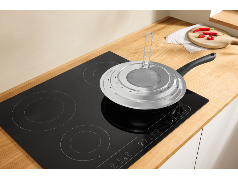 Frying pan with splatter guard on an induction hob in a kitchen with a wooden countertop.