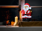 Christmas decoration with an illuminated Santa Claus, candles, and gifts on a windowsill.