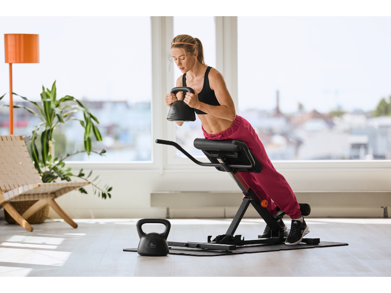 Woman exercising on a fitness bench with a black kettlebell in her hands.