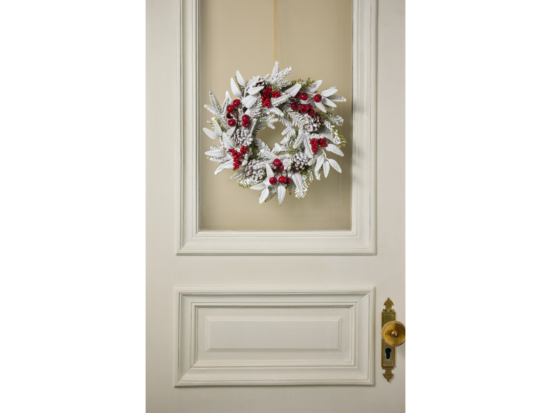 Flocked Christmas wreath with red berries and pinecones on a door.