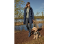 Woman in navy rain jacket and rubber boots walks dog in leopard print jacket by lake.