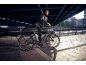Man in sportswear on an electric bike under a bridge.