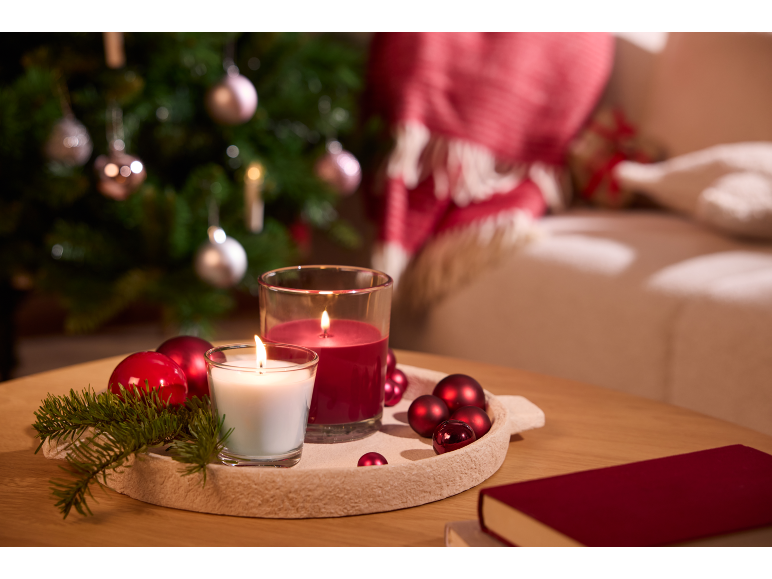Christmas decoration with red and white candles, baubles, and a Christmas tree in the background.