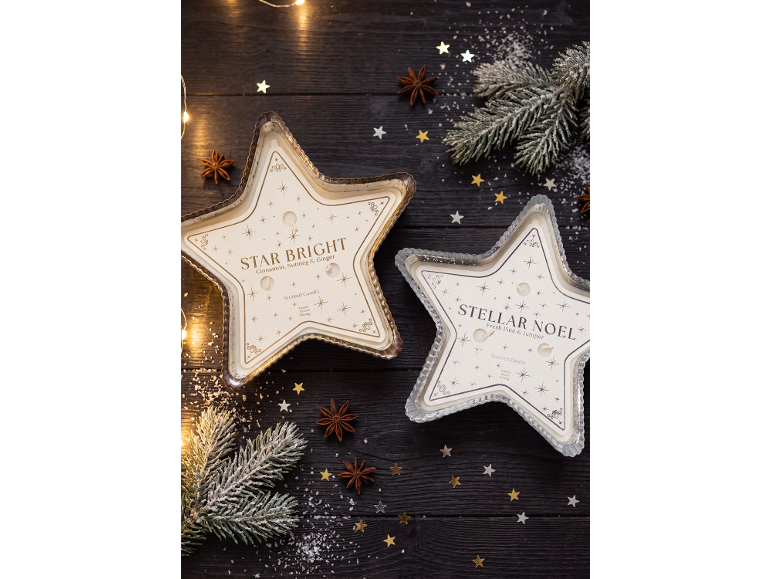 Two star-shaped scented candles on a wooden background with Christmas decorations.