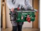 Man holding a green and black table saw with red details.