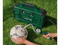 Green air compressor inflating a white soccer ball on grass, with a person holding the ball and pressure gauge.