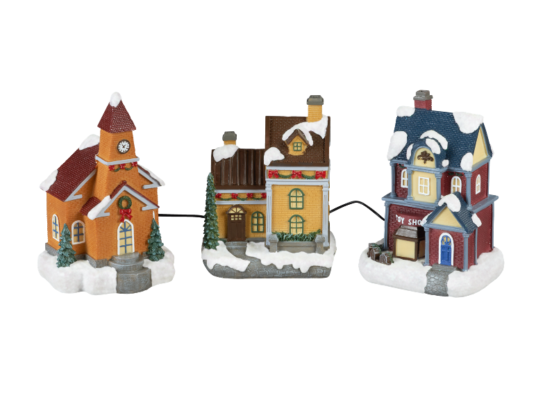 Christmas village set with church, house, and toy shop, covered in snow.