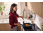 Woman cooking chicken in a grill pan on an induction hob in a modern kitchen.