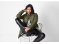 Woman in green puffer jacket and black faux leather leggings, sitting on a chair.