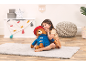 Girl hugging a teddy bear with a red hat and blue coat, sitting on a rug.