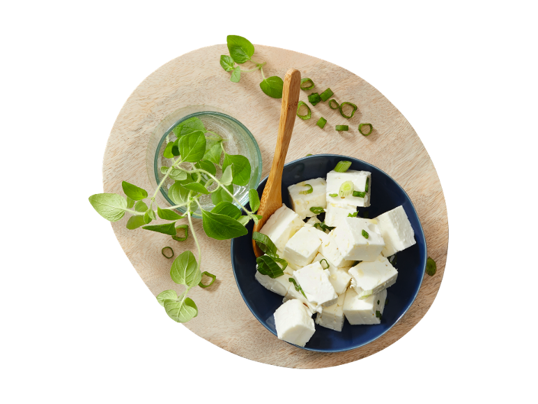 Feta cheese cubes with fresh oregano and chopped spring onions on a wooden board.