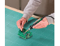 Man soldering a circuit board with a soldering iron and tweezers on a cutting mat.
