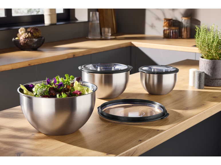 Stainless steel mixing bowls with lids, one filled with salad, on a kitchen counter.