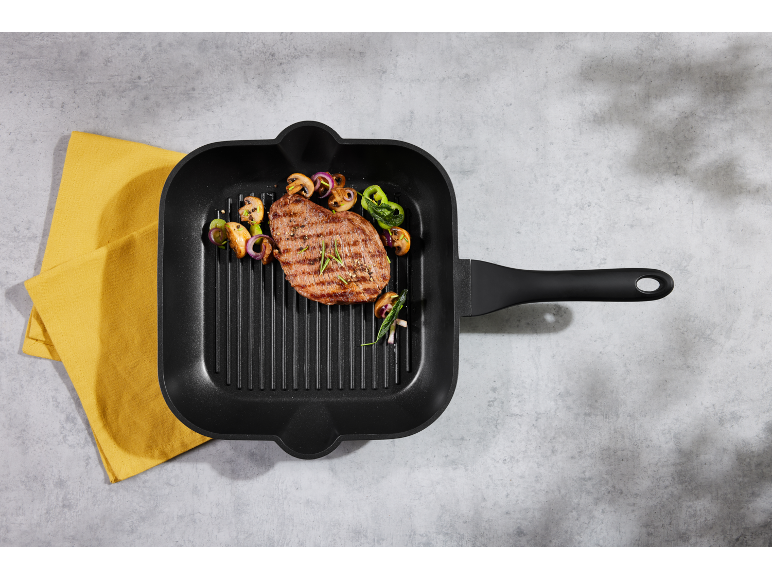Grilled steak with vegetables in a black grill pan on a gray background with a yellow towel.