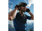 Man in cycling helmet, sunglasses, and gloves, with a mountain landscape in the background.