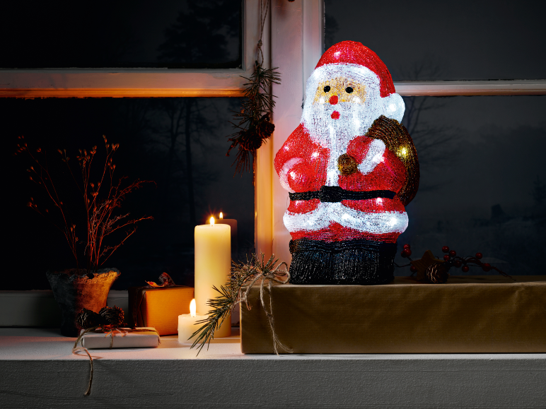 Christmas decoration with an illuminated Santa Claus, candles, and gifts on a windowsill.