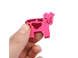 A hand holding a small pink wooden cow figurine against a white background.