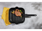 Grilled steak with vegetables in a black grill pan on a gray background with a yellow towel.