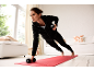 Woman in black tracksuit exercising with dumbbells on a red exercise mat.