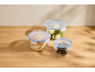 Three Silvercrest glass food containers with blue lids, filled with food, on a wooden surface.