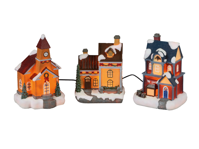 Lit Christmas village houses and church covered in snow, with garlands and wreaths.