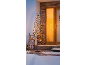 Lit Christmas tree in front of a house with snow and wood.