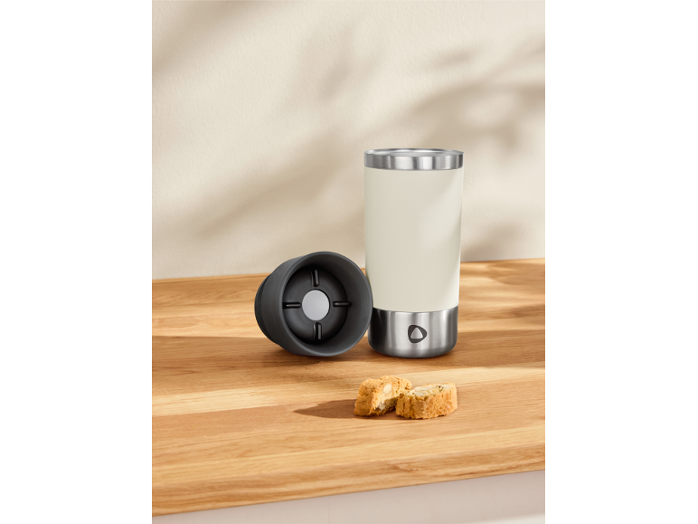 A cream-colored travel mug with a black lid and two biscotti on a wooden surface.