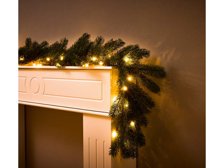 Christmas garland with warm white LED lights draped over a white fireplace.