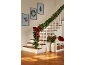 Christmas garland with lights and a red bow decorating a staircase, with festive wall art.