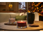 Two lit candles on a wooden table, with a vase of berries and blurred lights in the background.