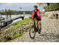 Woman on an e-bike on a paved road by a river.