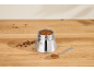 Moka pot filled with ground coffee, coffee beans, and a spoon on a wooden table.