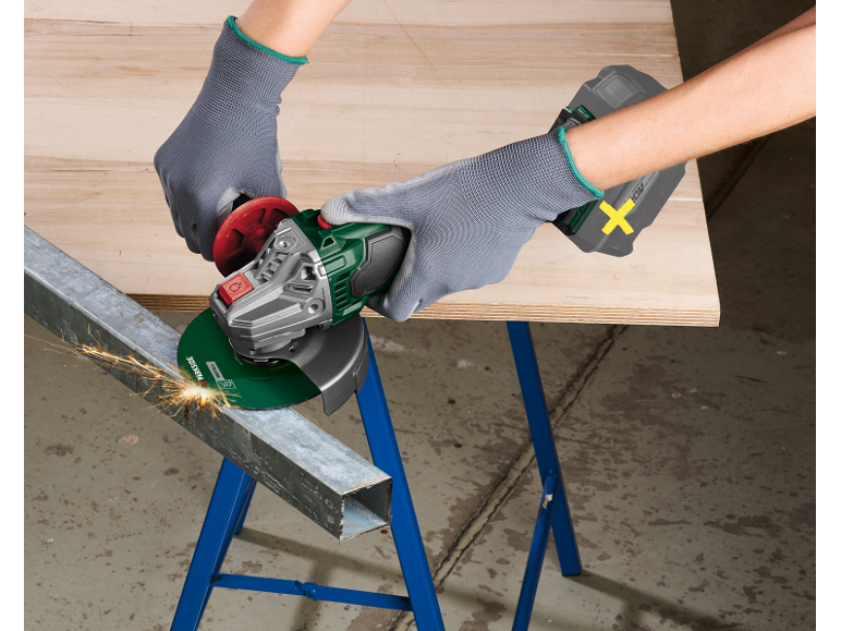 Gloved person using an angle grinder to cut a metal beam, sparks flying.