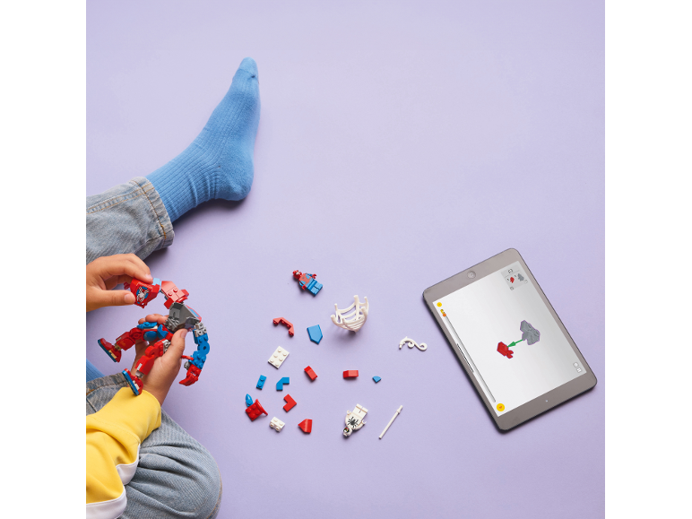 A child plays with superhero building blocks, following instructions on a tablet.