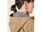 Woman in beige hooded raincoat and patterned blouse, gold earring.