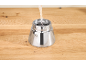 Water being poured into the silver base of a coffee maker on a wooden table.