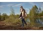 Woman in a beige raincoat and blue wellington boots walks by a lake.