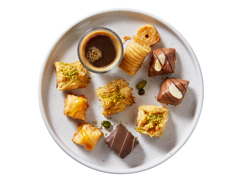 Plate of assorted sweets, including pistachio and honey baklava, chocolates, and coffee.
